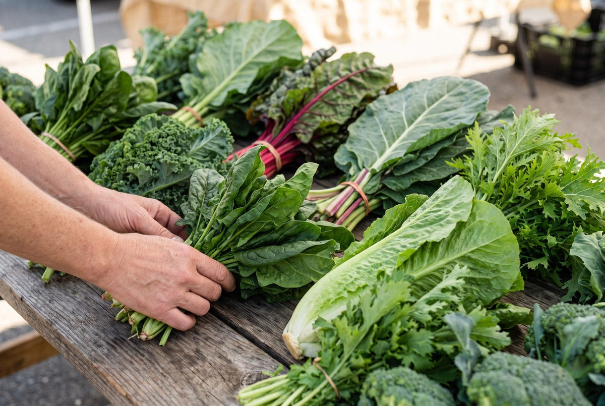 Bunches of spinach, Swiss chard, collards and kale on a wooden cutting board with a bowl of green peas